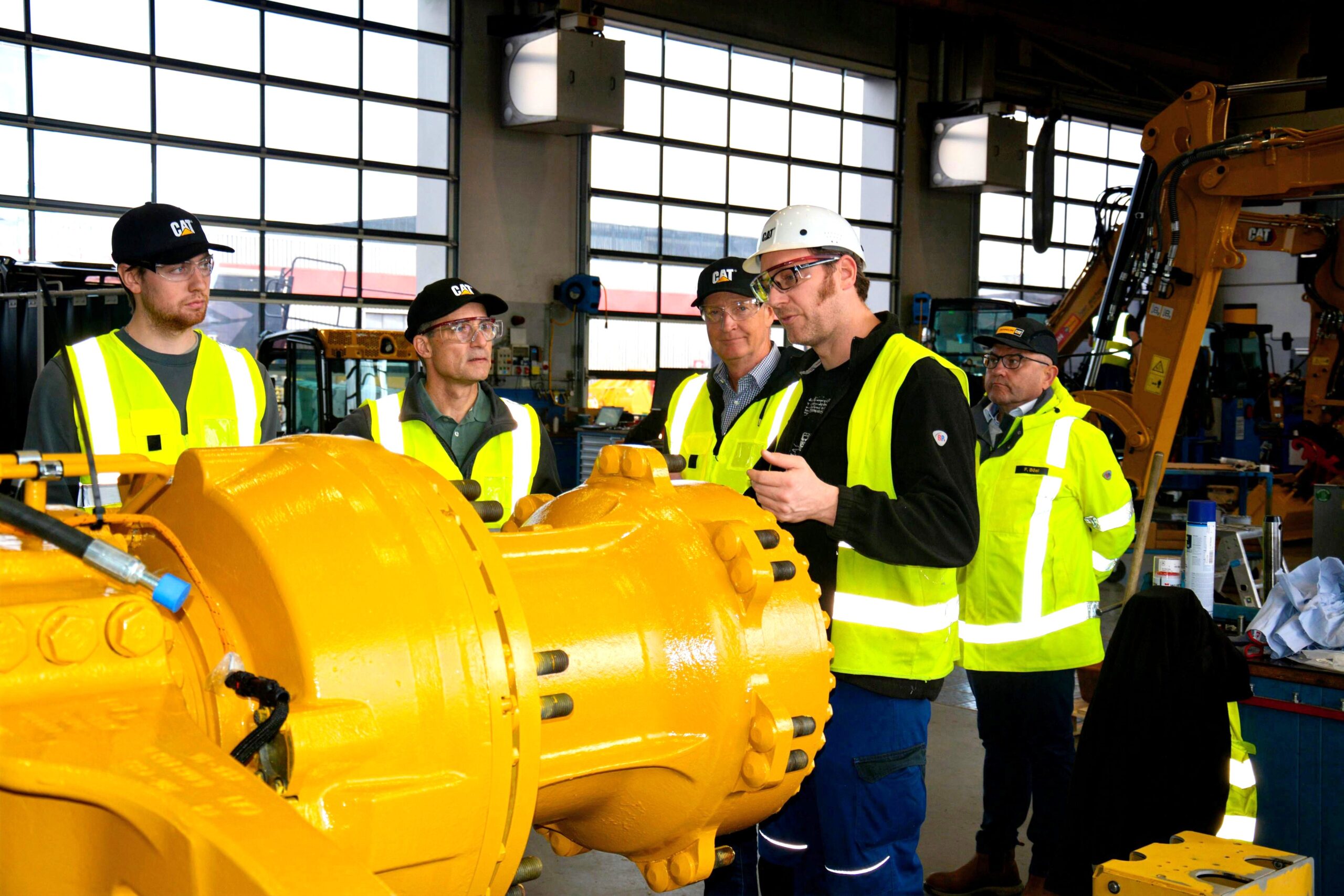 Beim Werkstattbesuch erläuterte Andreas Binner (Zweiter von rechts), stellvertretender Werkstattleiter der Zeppelin Niederlassung Garching, Florian Schwinger (links), Dr. Kristian Daub (Zweiter von links) und Jörg Schwinger (Dritter von links), wie der Cat Muldenkipper 775 Schritt für Schritt in den neuwertigen Zustand versetzt wird. Copyright: Zeppelin