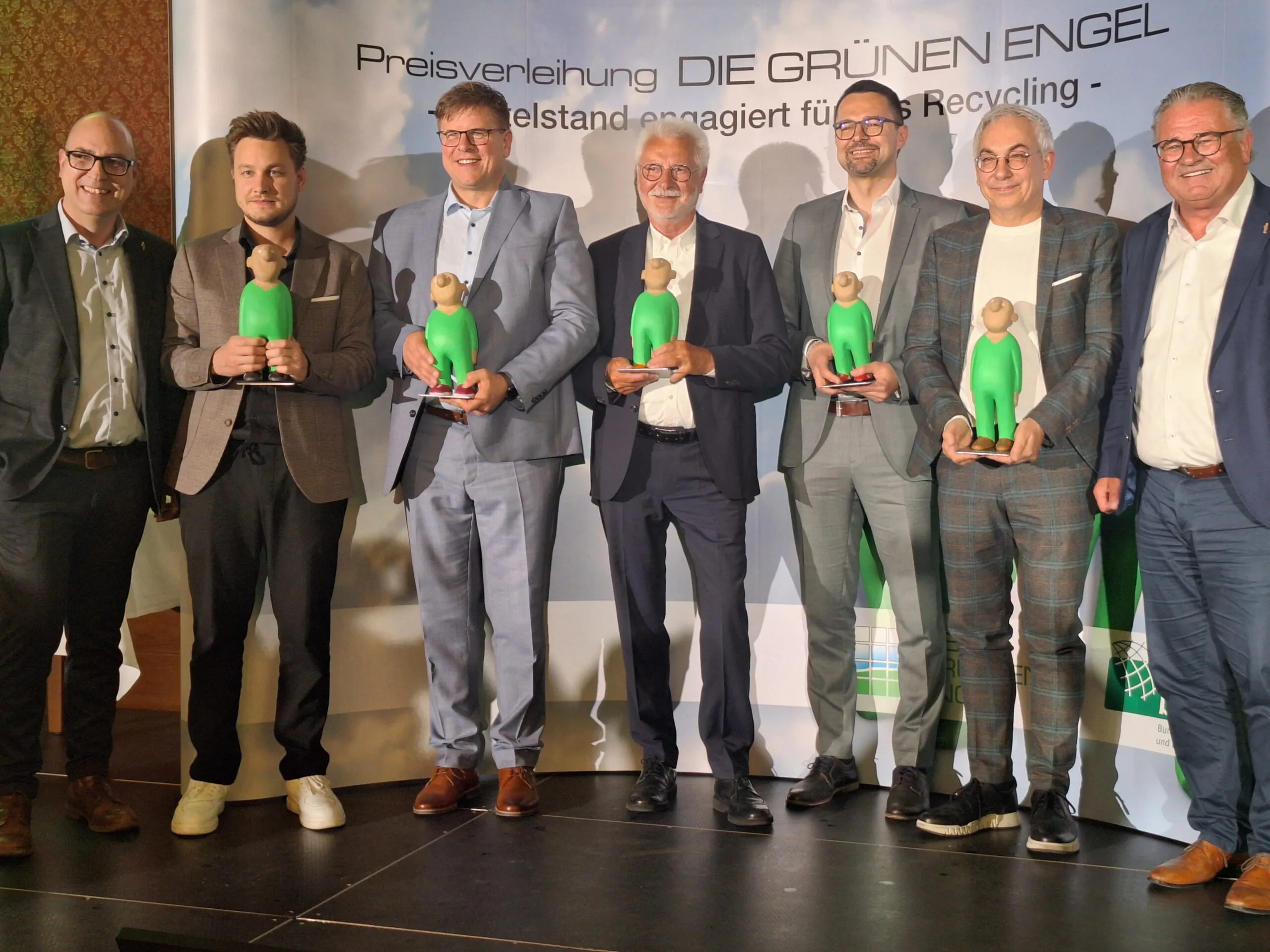 Ausgezeichnet mit dem GRÜNEN ENGEL 2026 wurden Alexander Korn (Korn Recycling GmbH, 3. v. links) und Nathanael Laier (WeSort.AI, 2. von links). Sie nahmen neben anderen Preisträgern den Preis als Gewinner in der Kategorie „Zukunftsweisende Techniklösung“ für die gemeinsame Entwicklung einer KI-gestützten Lösung zur deutlichen Senkung von Brandrisiken im Recycling entgegen.